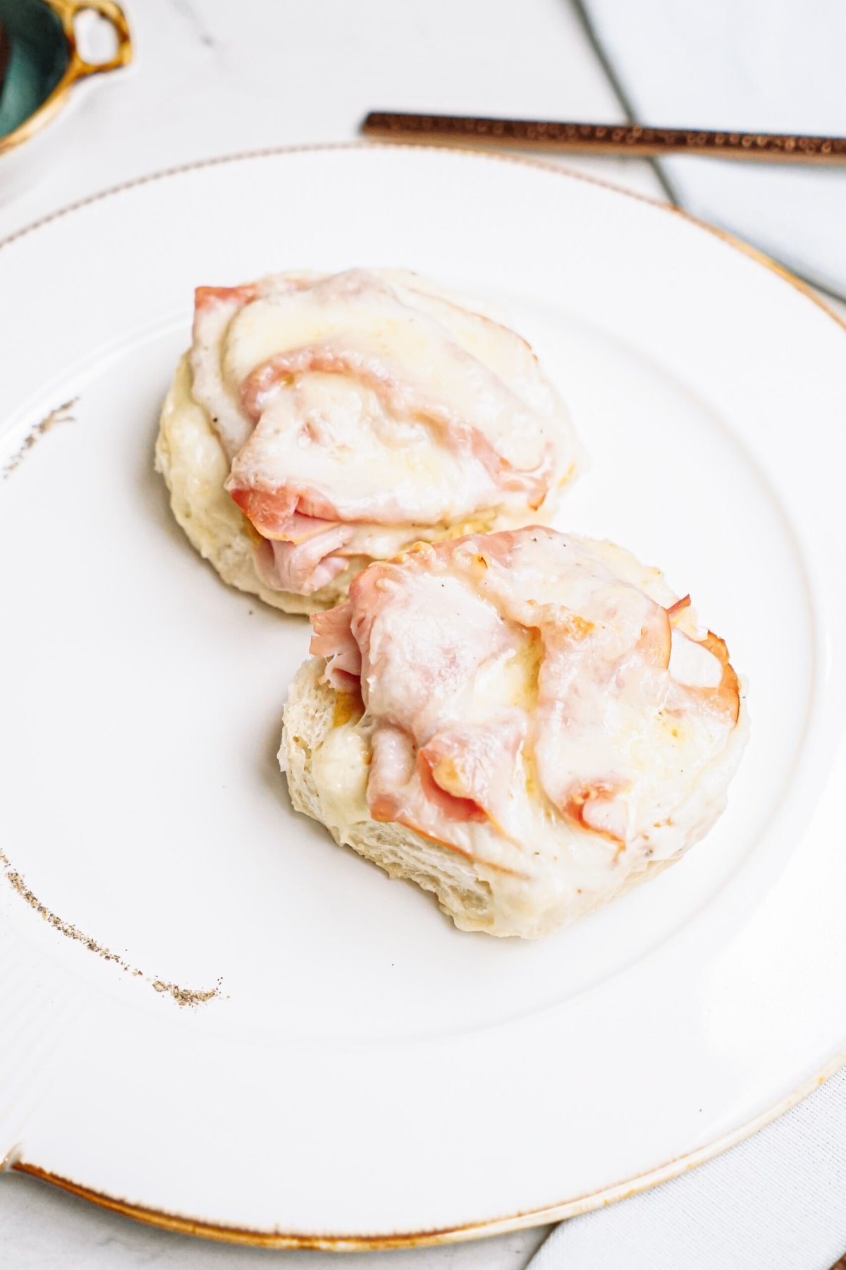 Two open-faced baked sandwiches with ham and melted cheese on a white plate.