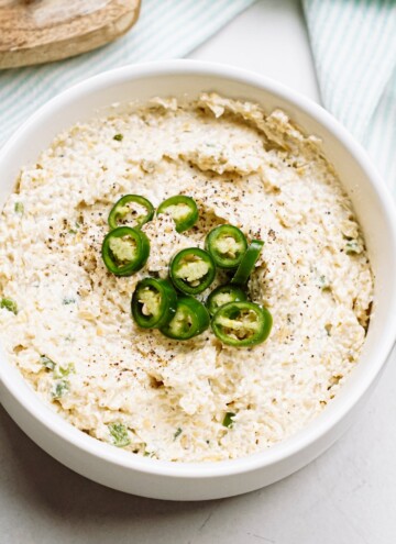 jalapeno artichoke dip in a serving bowl with sliced jalapeños on top
