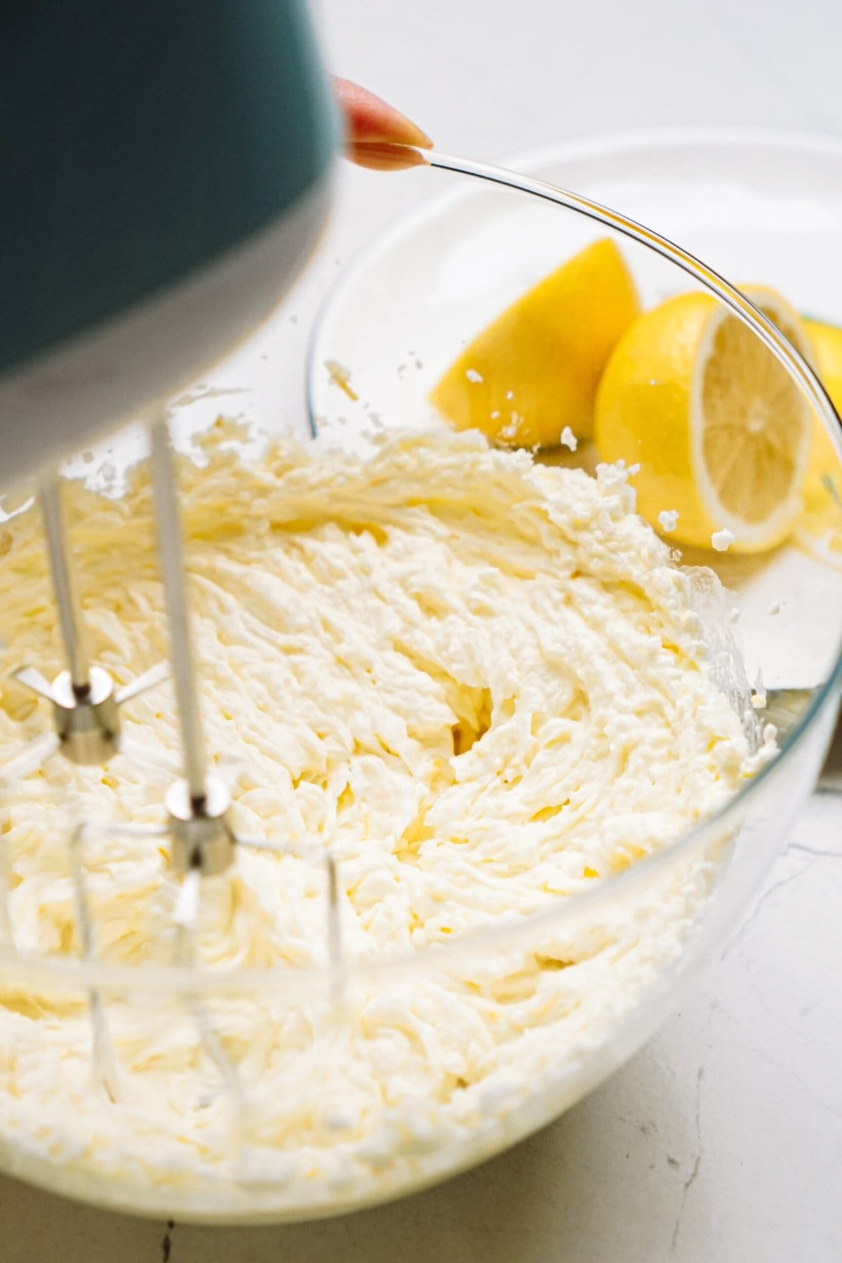 Electric mixer whipping cream in a bowl with cut lemons in the background.