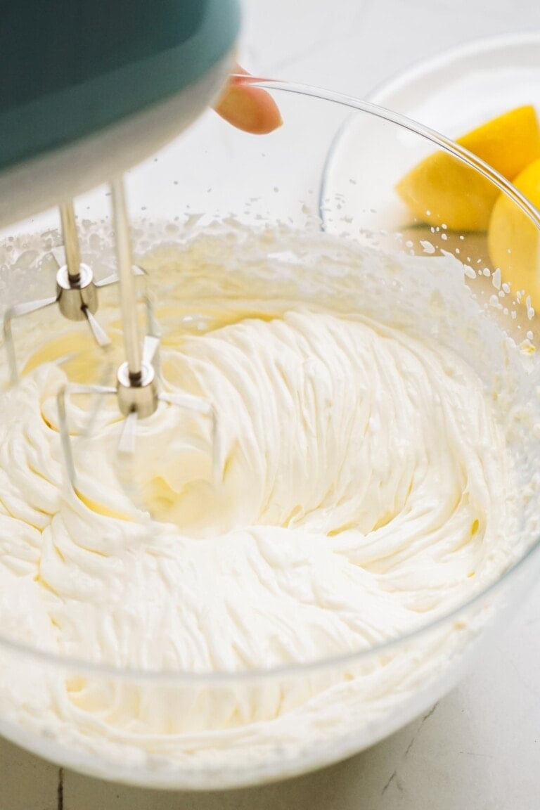 A hand mixer blending ingredients into a smooth cream in a glass bowl.