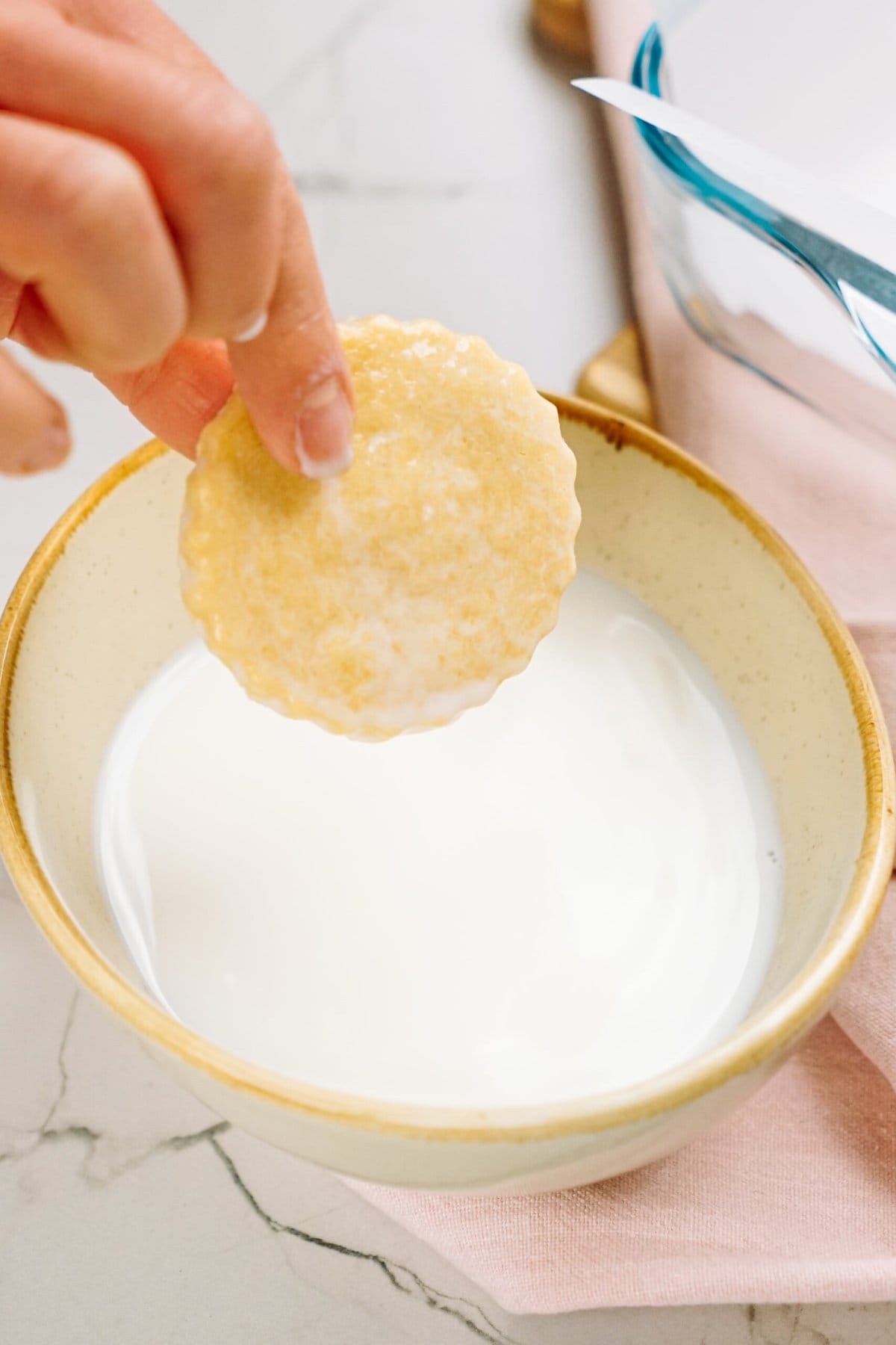A hand dipping a shortbread cookie into a bowl of milk.