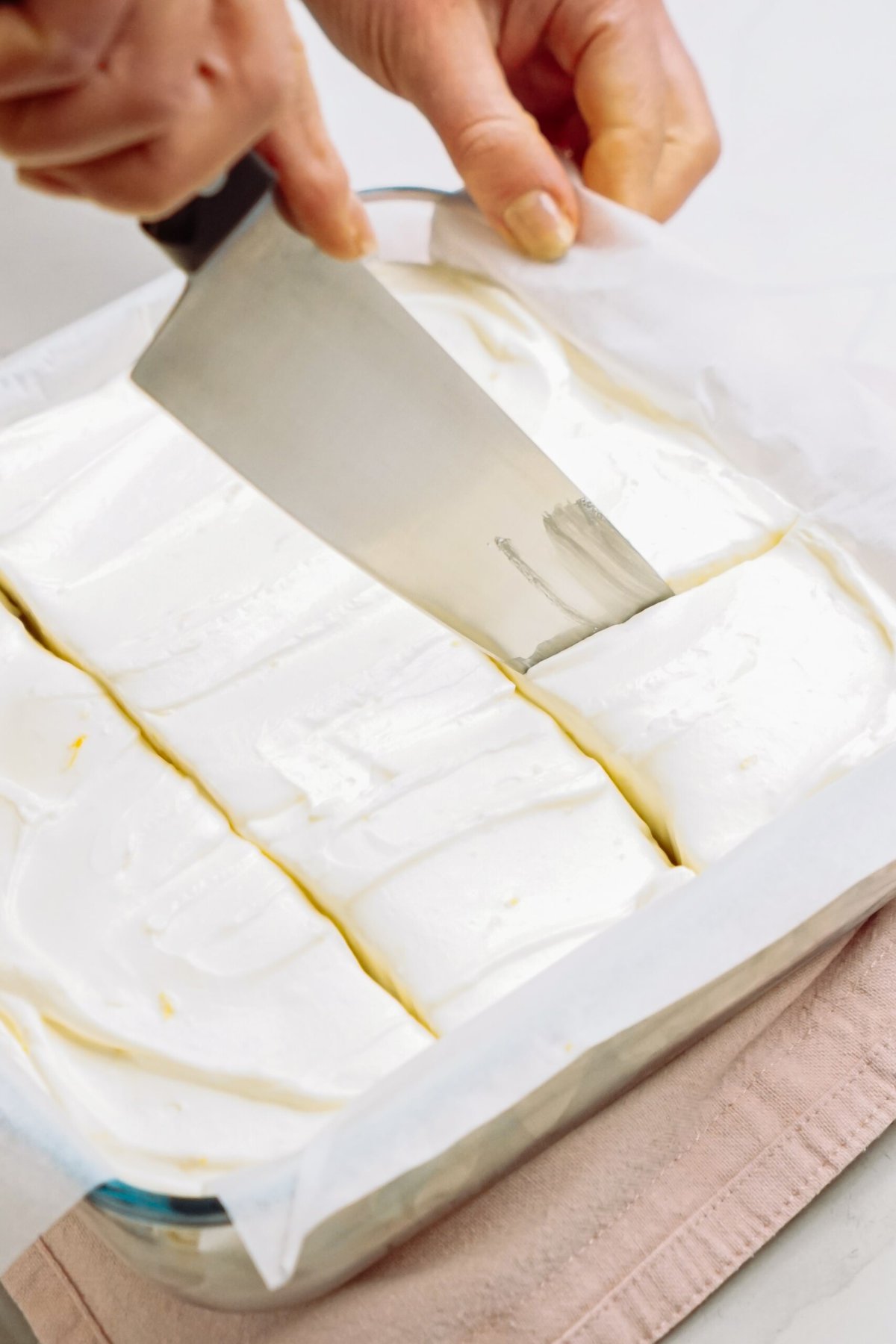 Slicing a lemon icebox cake in a tray with a metal spatula.