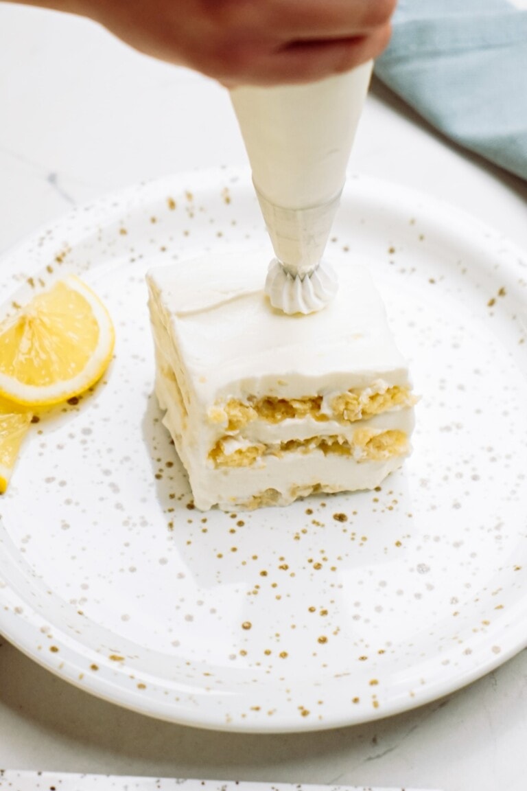 Icing being piped onto a layered lemon dessert on a decorated plate.