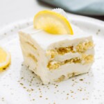 A slice of lemon dessert with creamy layers on a plate, garnished with a lemon slice and zest.