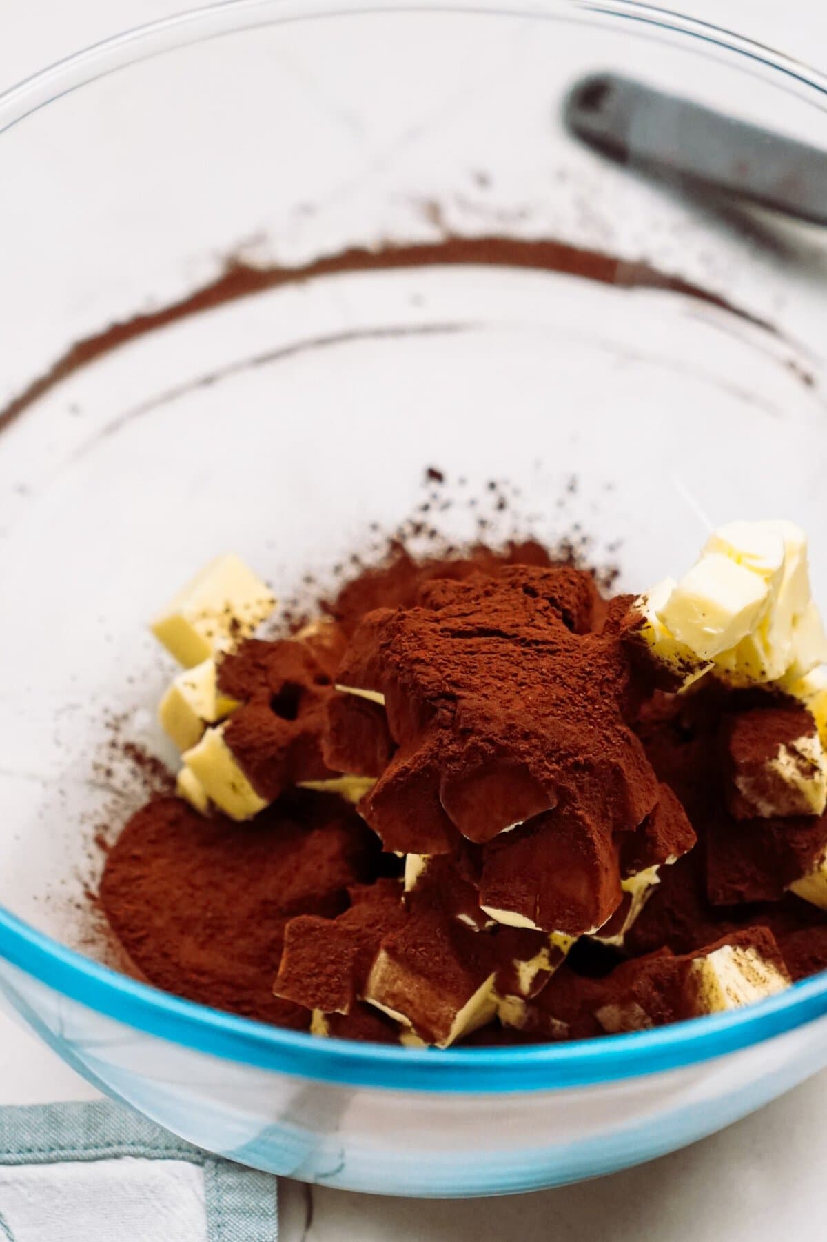 Cubed butter and cocoa powder in a glass mixing bowl.