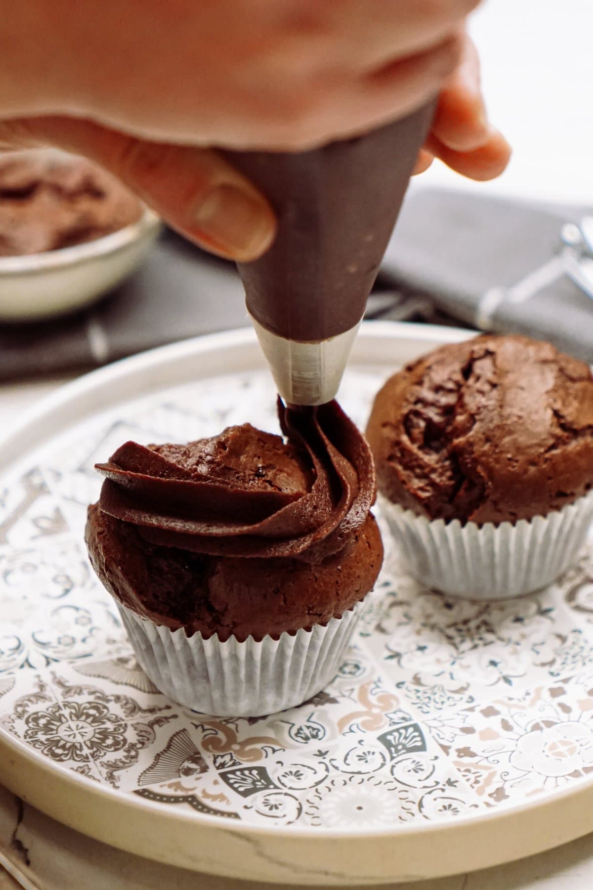 Applying chocolate frosting to a cupcake with a piping bag.