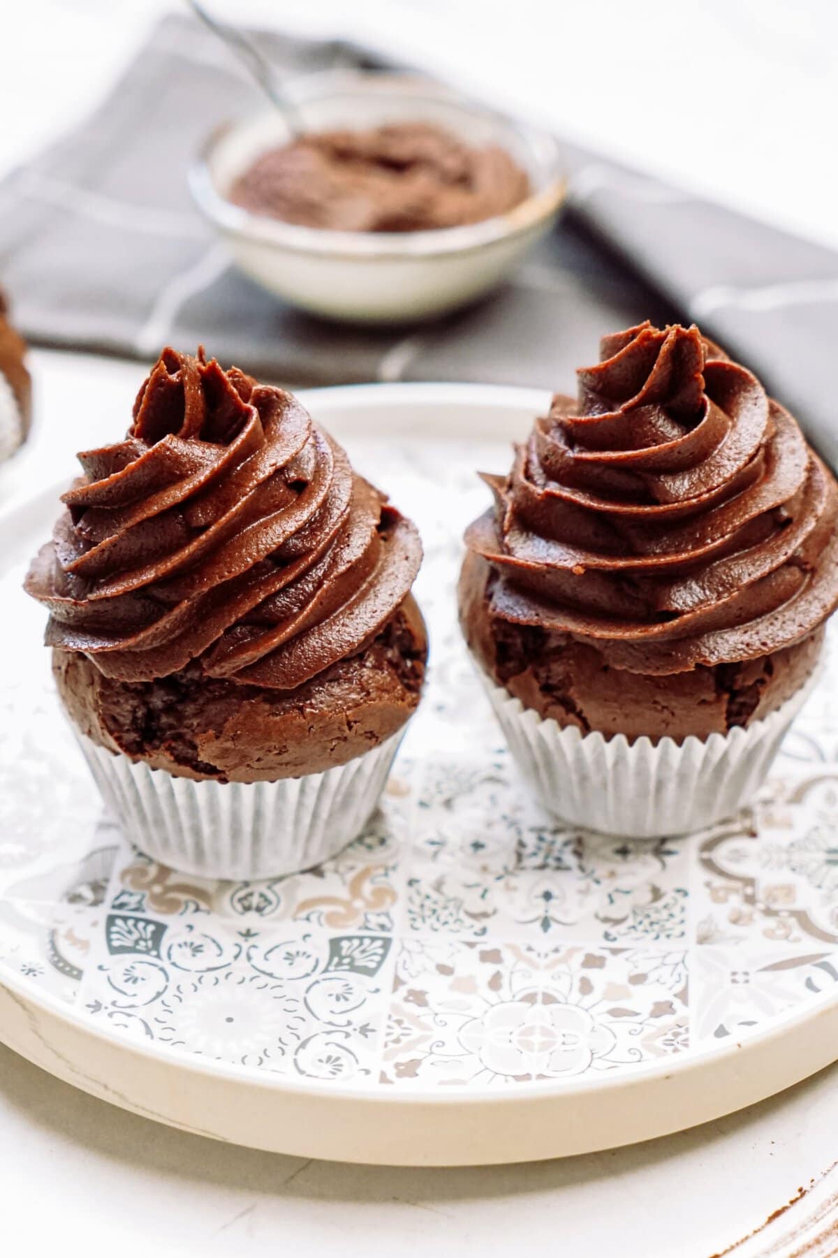 Two chocolate cupcakes with swirled frosting on a decorative plate.
