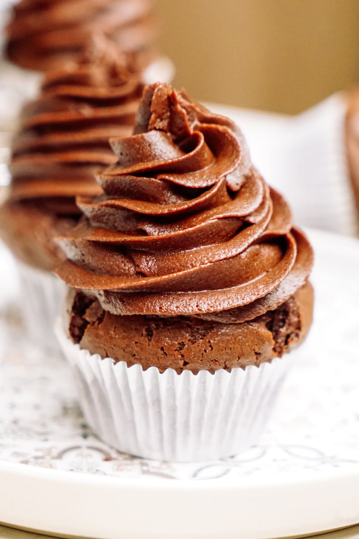 A chocolate cupcake with a swirl of chocolate frosting on a plate with a floral pattern.