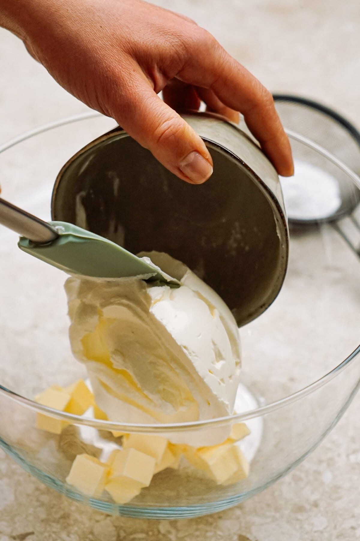 a person adding cream cheese to the glass bowl with butter