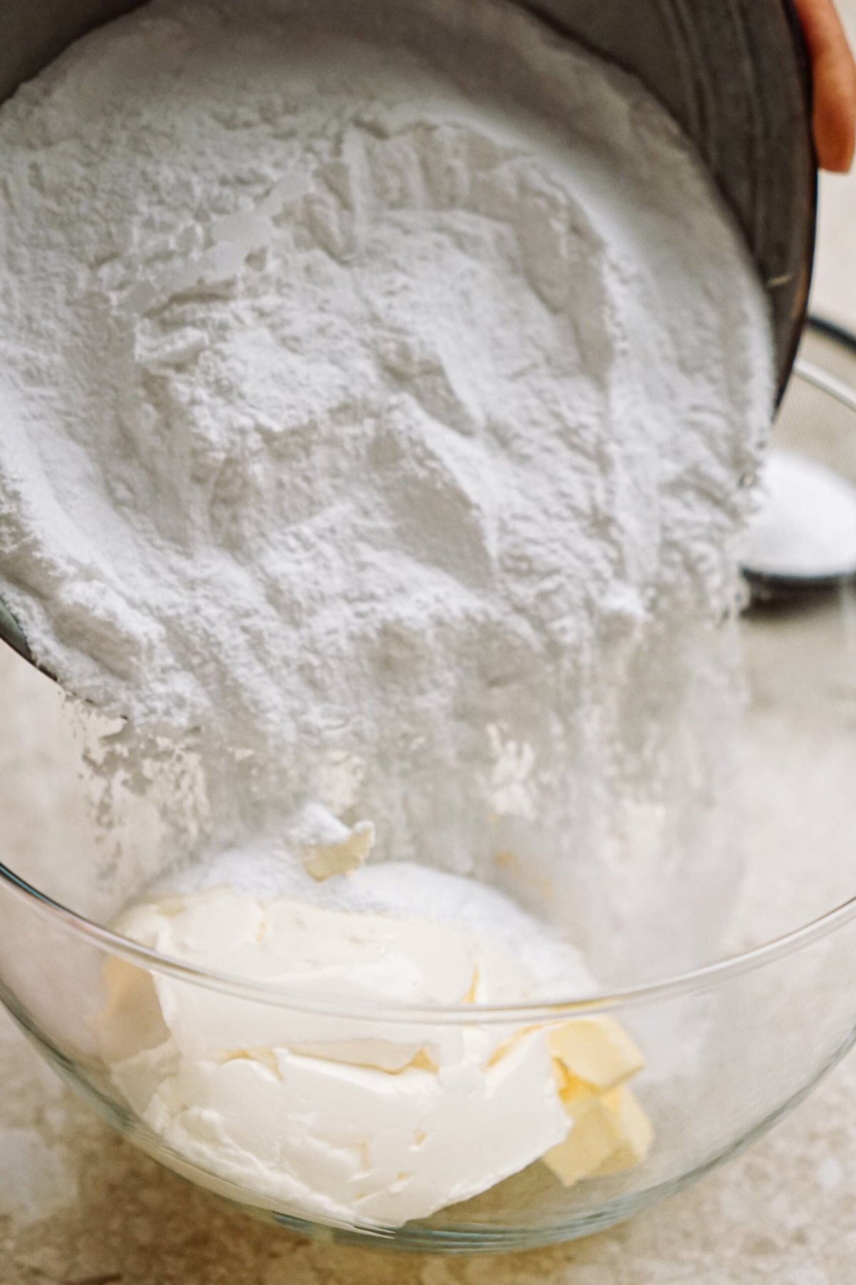 powdered sugar being added to glass mixing bowl