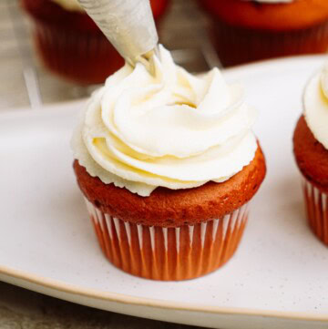 piping cream cheese frosting onto cupcakes
