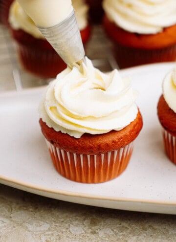 piping cream cheese frosting onto cupcakes