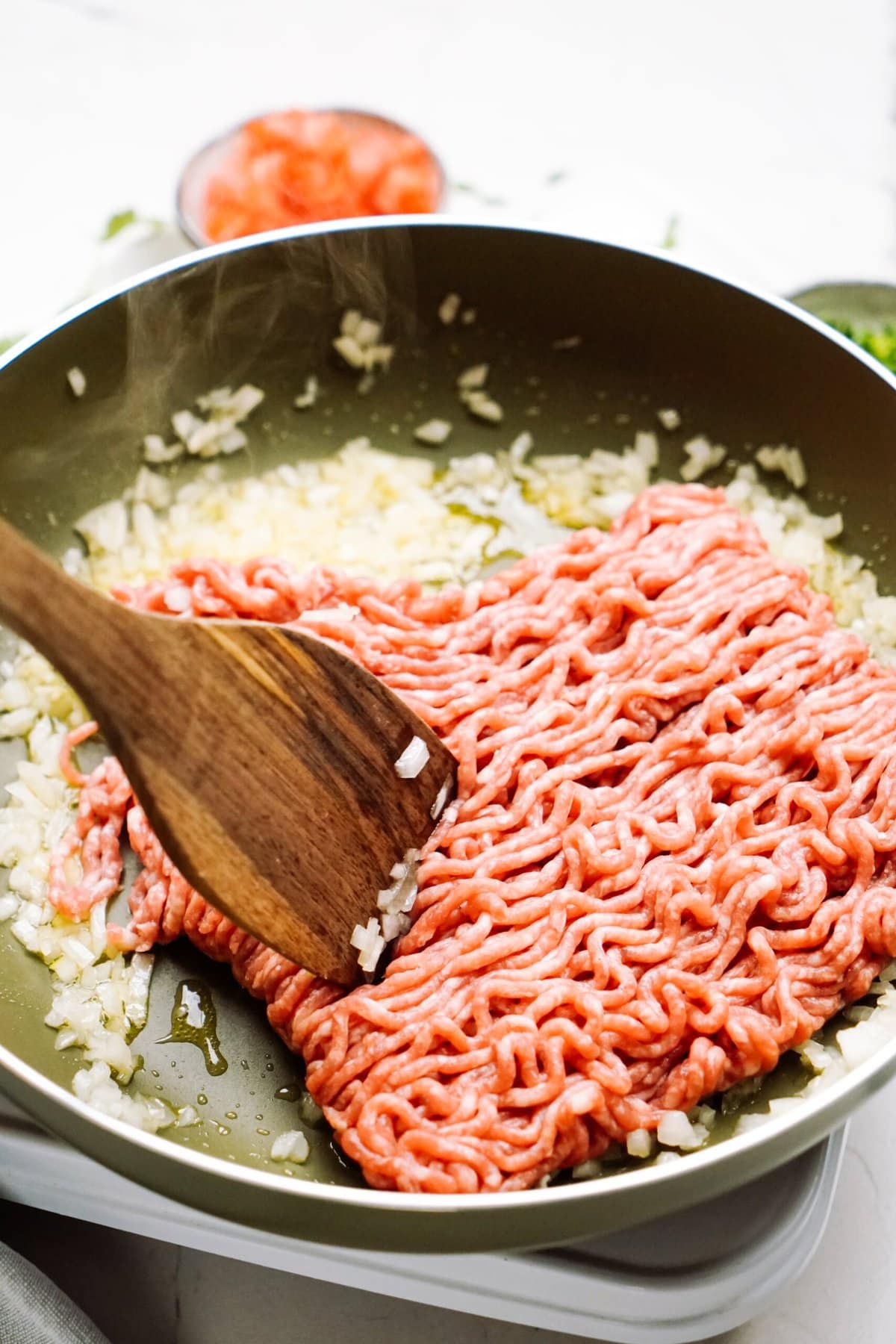 a person breaking apart ground beef to brown in a skillet 