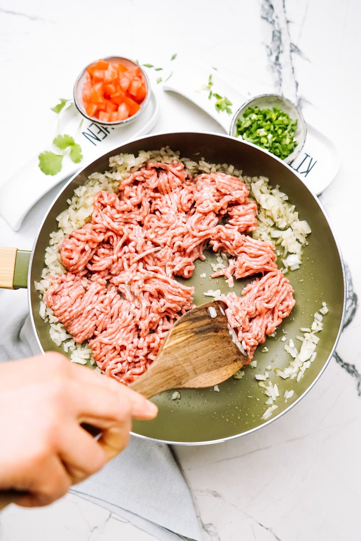 a person browning ground beef in a skillet with onions 