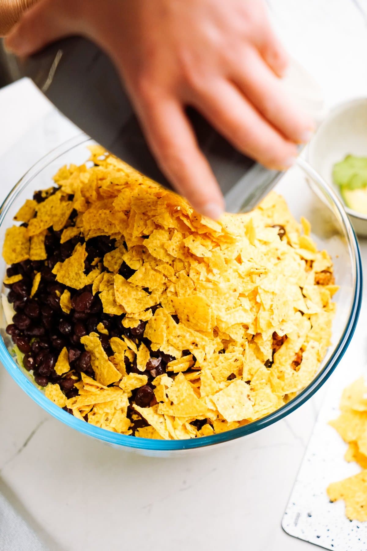 a person pouring crushed chips onto a bowl of taco 