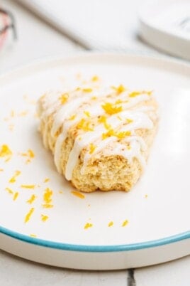 orange scone with glaze drizzled over the top on a plate