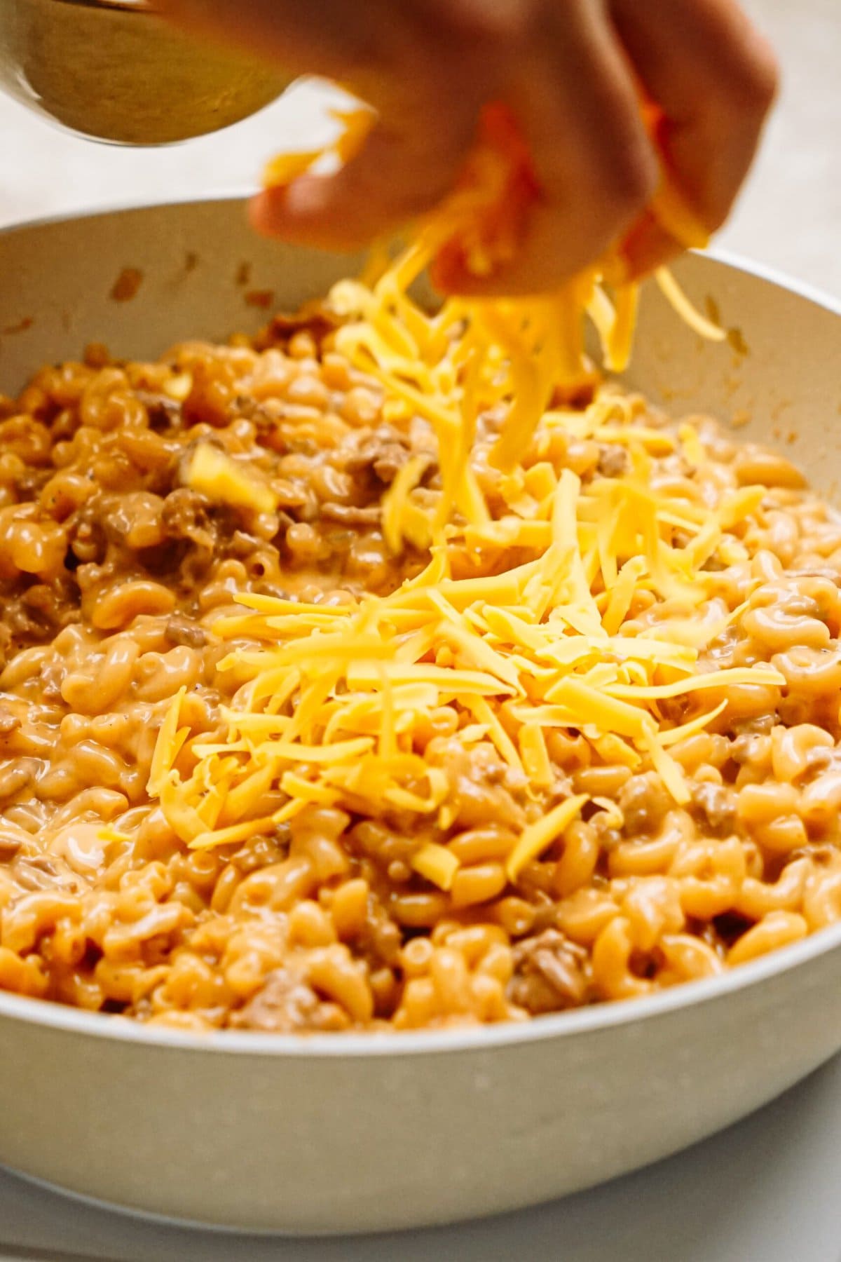 shredded cheese being sprinkled into the hamburger helper mixture 