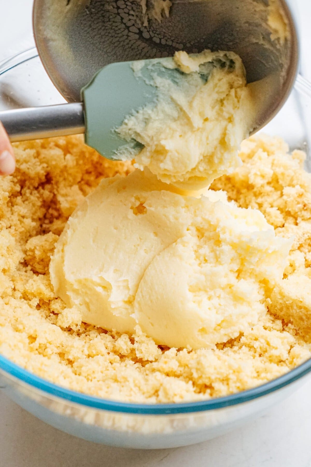 vanilla frosting being added to crumbled cake in a mixing bowl 