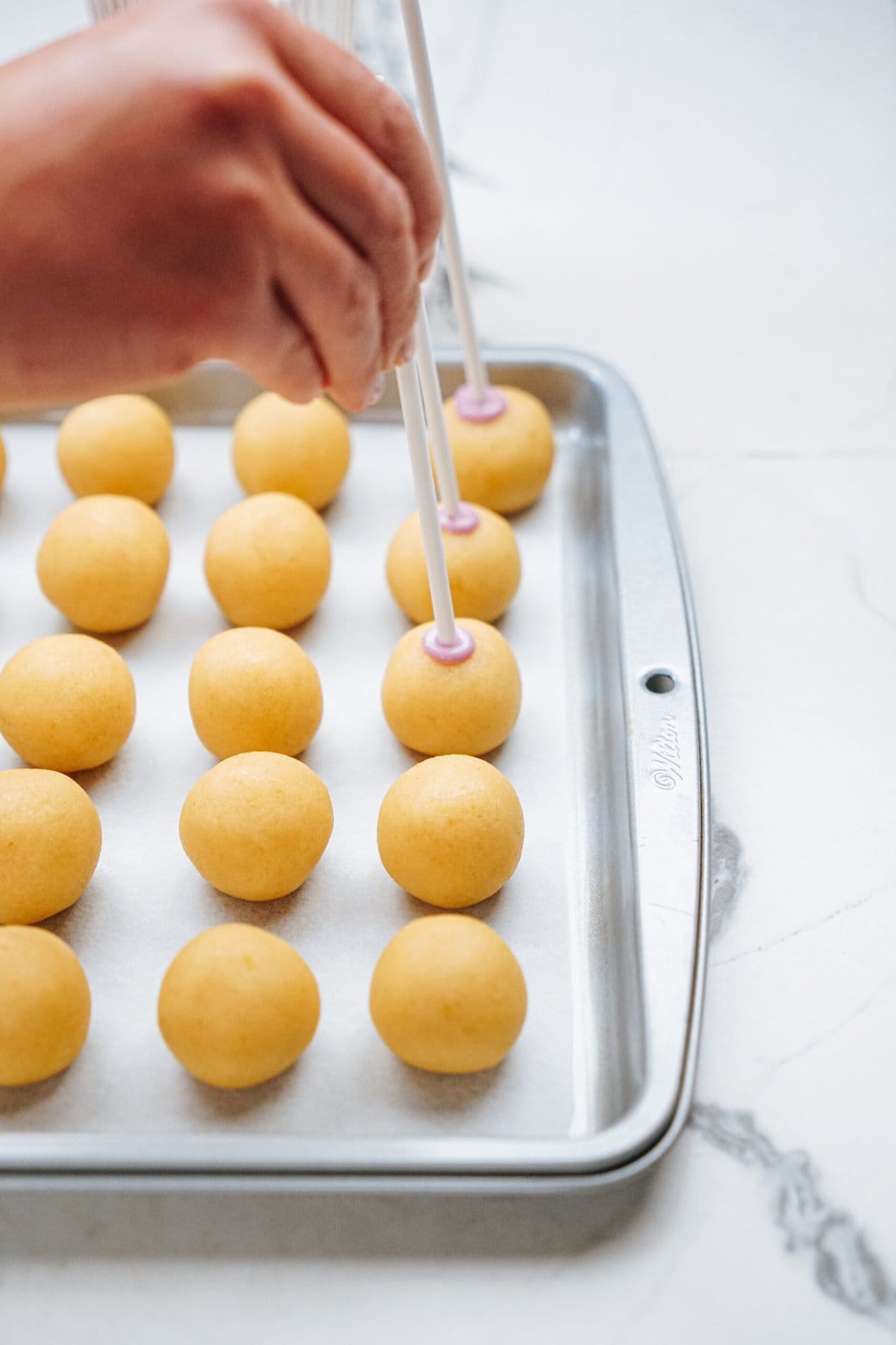 a person inserting cake pop sticks into each cake ball 