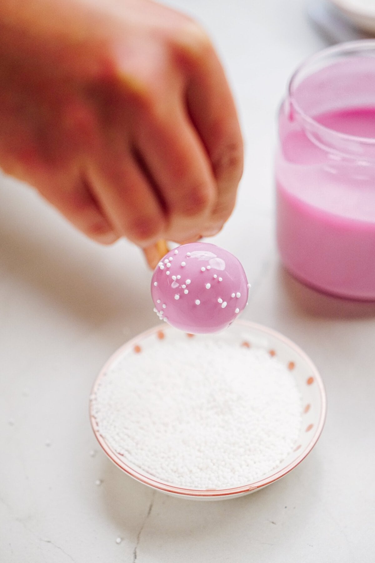 a person adding white sprinkles to a cake pop