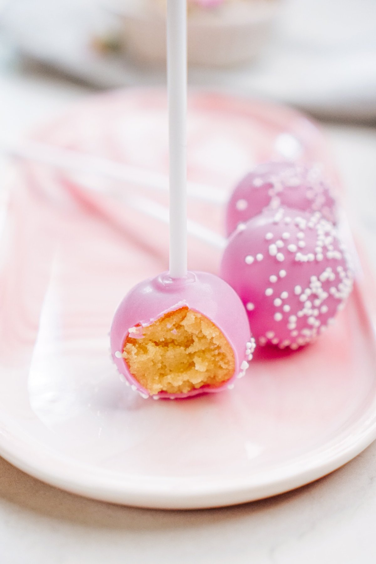 3 cake pops on a plate, one with a bite taken