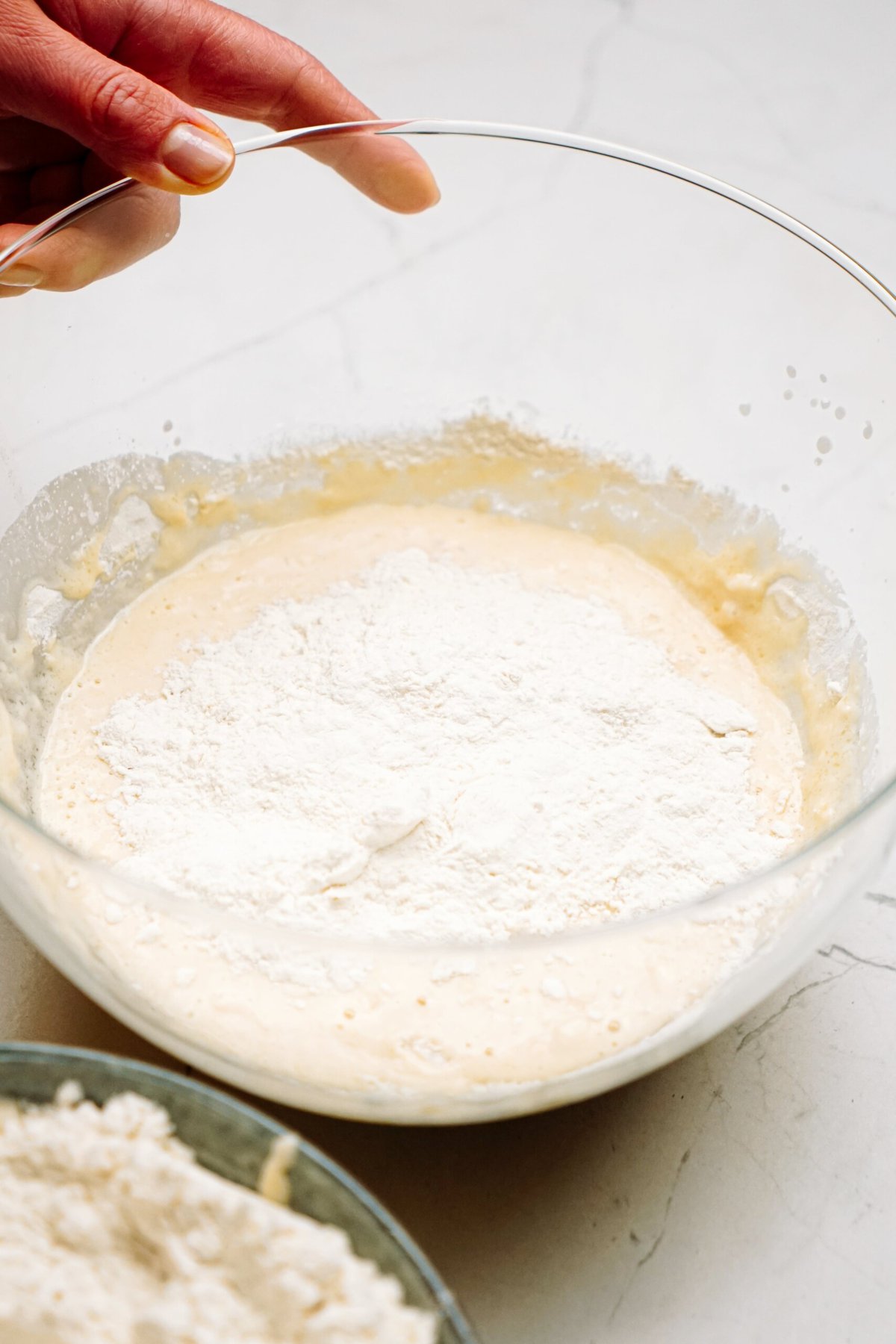 flour added to a yeast mixture in a glass mixing bowl 