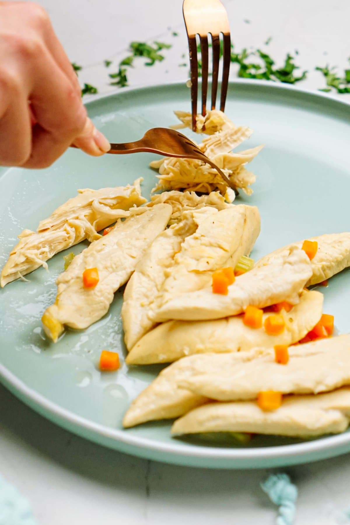 a person using two forks to shred chicken tenders on a plate 