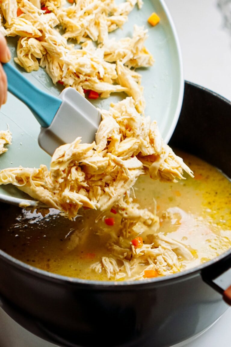adding shredded chicken to a pot of broth