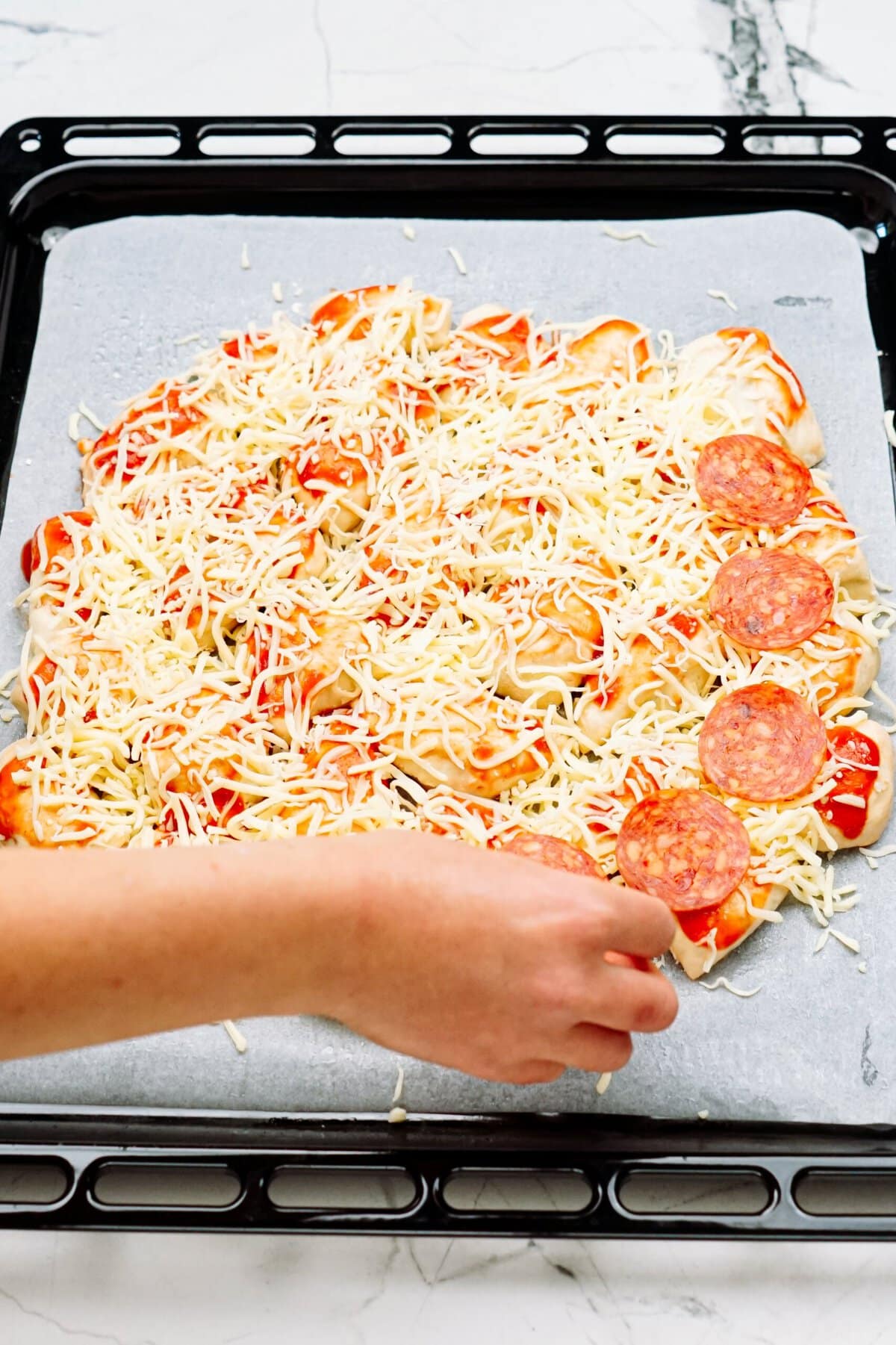 a person adding pepperoni to a pizza 