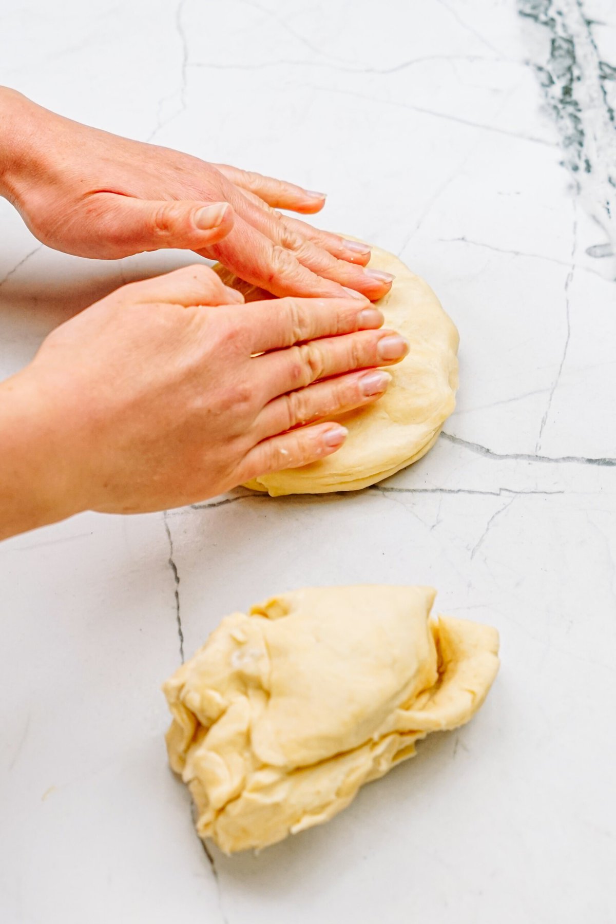 a person flattening half the dough into a disc