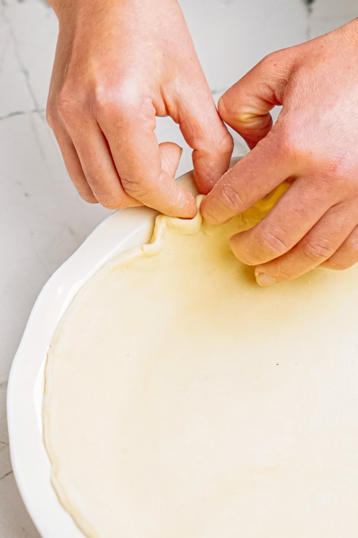 a person crimping the edge of the pie dough with their fingers