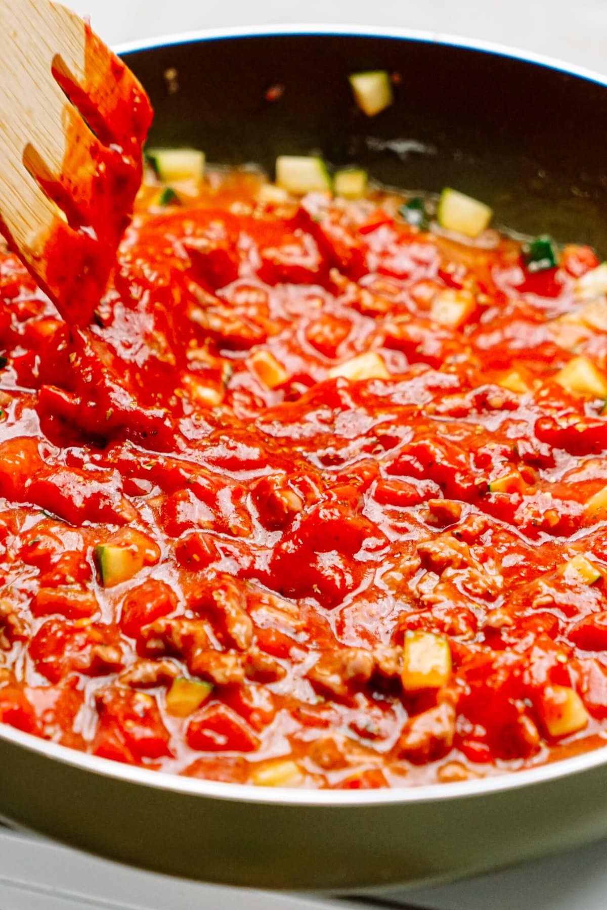 A pan filled with a chunky tomato-based sauce being stirred with a wooden spatula.