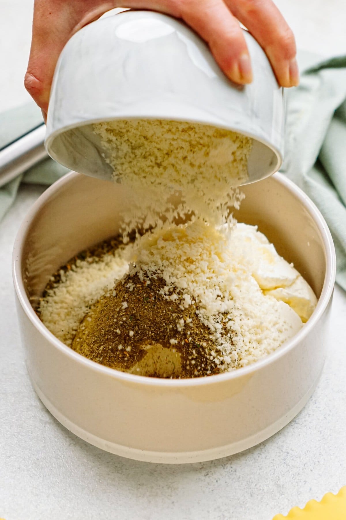 A hand is pouring breadcrumbs and seasonings into a mixing bowl with other ingredients.