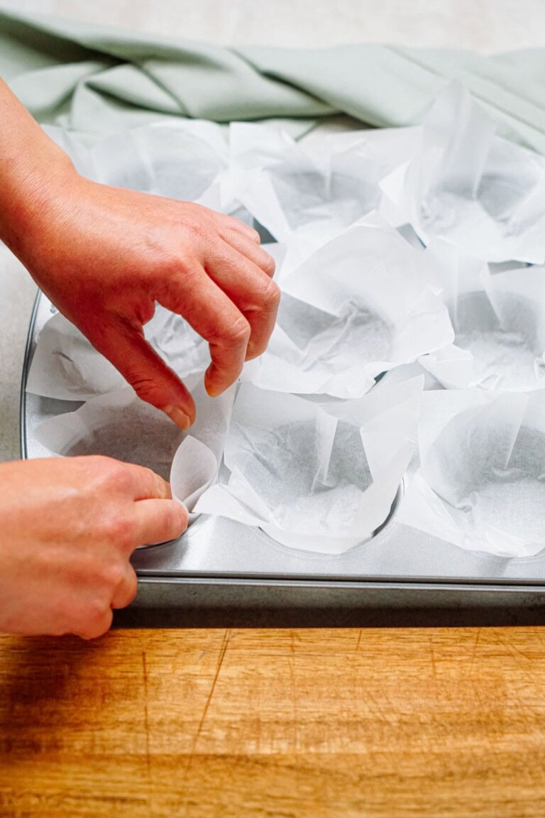 Hands lining a muffin tin with parchment paper.