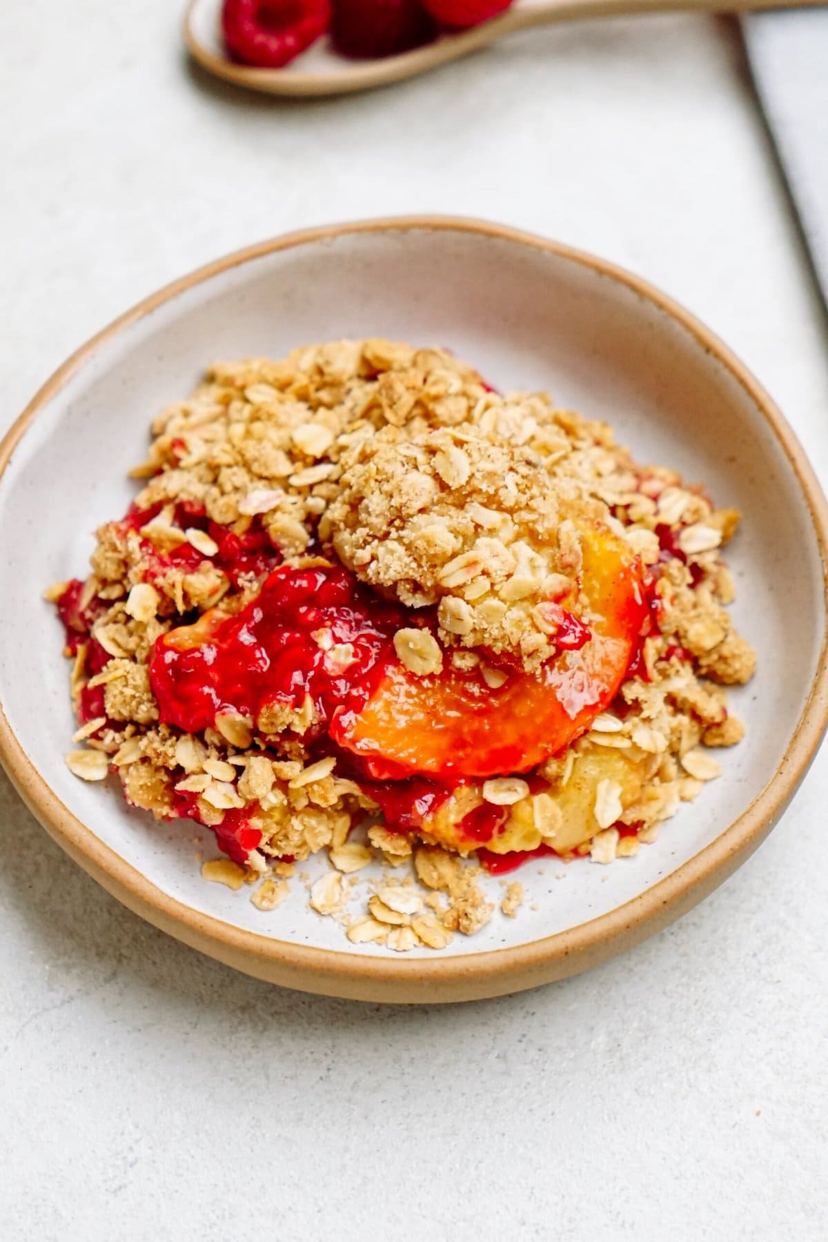 A plate of peach and raspberry crumble with a spoonful of raspberries in the background resembles a delightful raspberry cobbler.