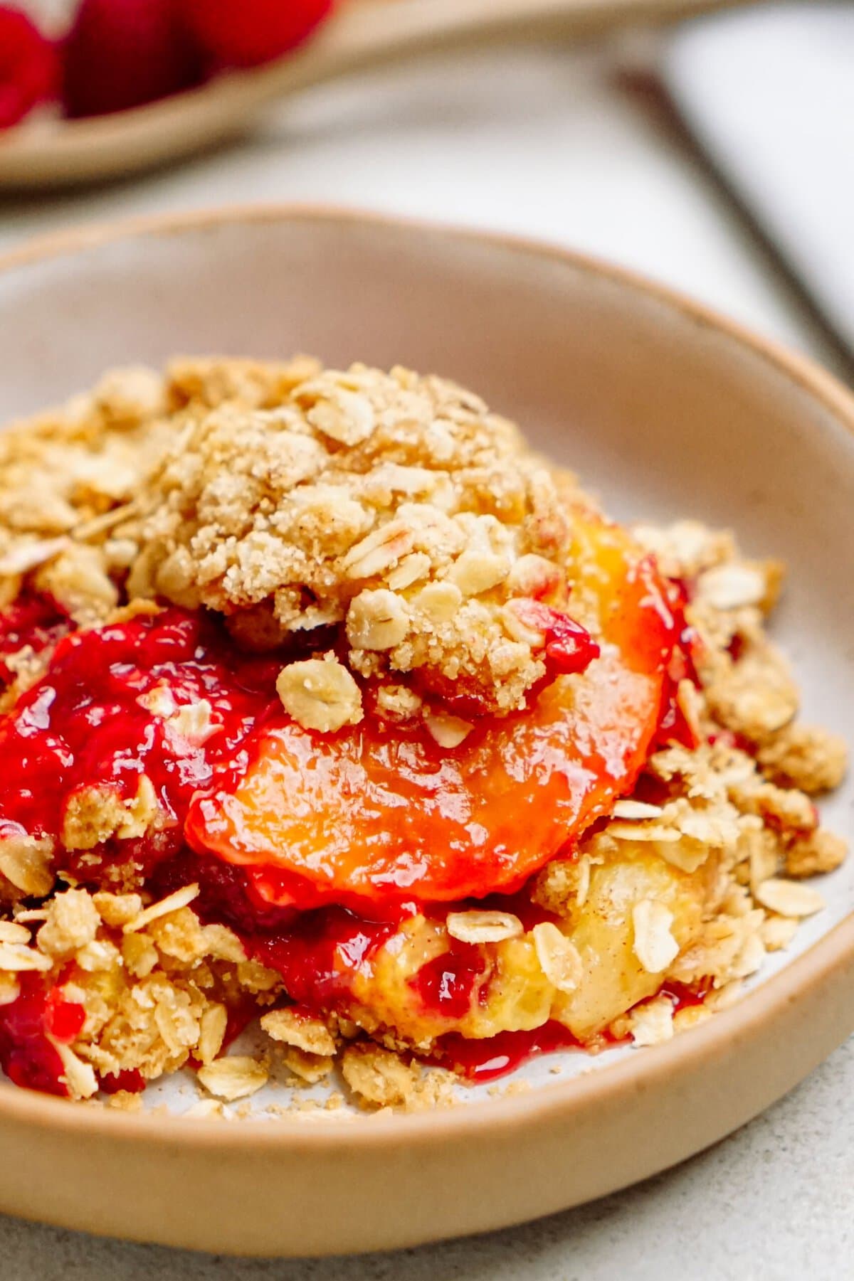 A close-up of a raspberry cobbler with a topping of oats and a mix of red and yellow fruit slices in a bowl.