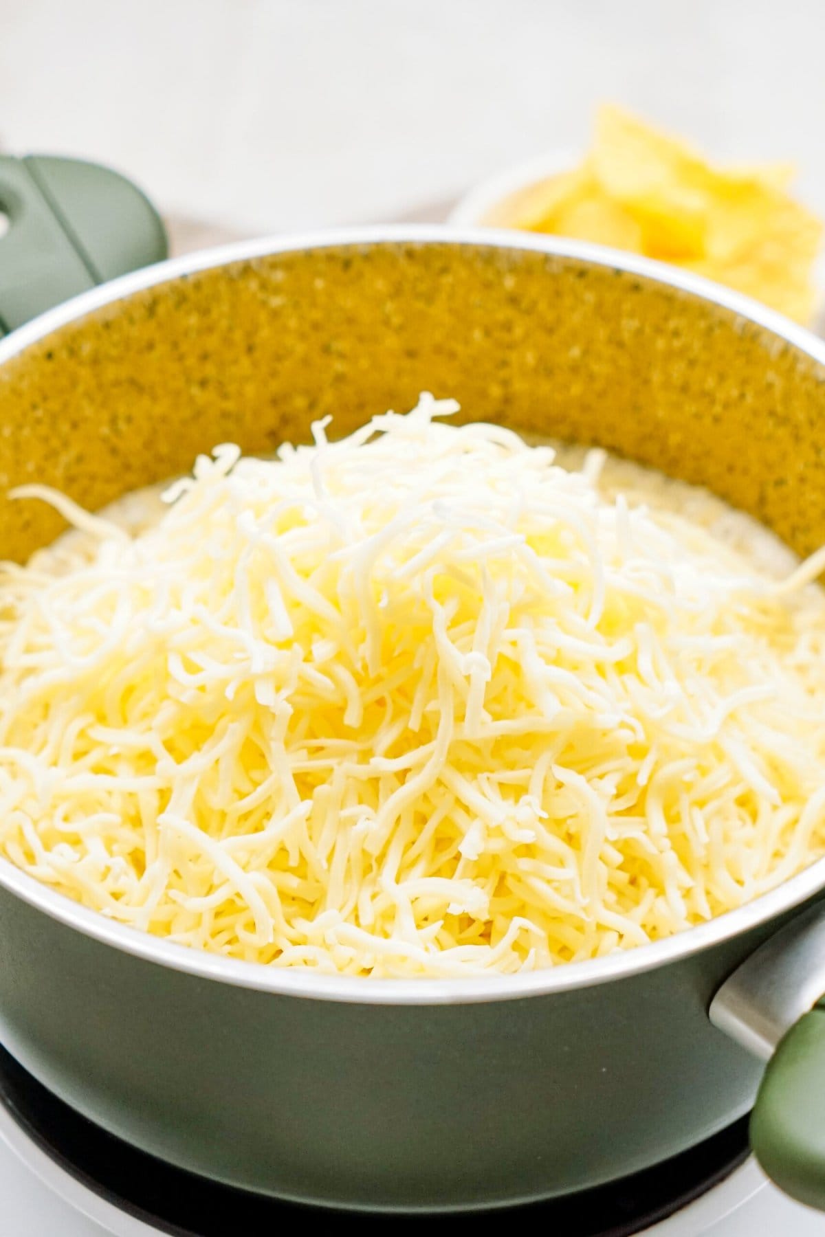 A pot filled with a generous amount of shredded cheese, with a small bowl of queso dip in the background.