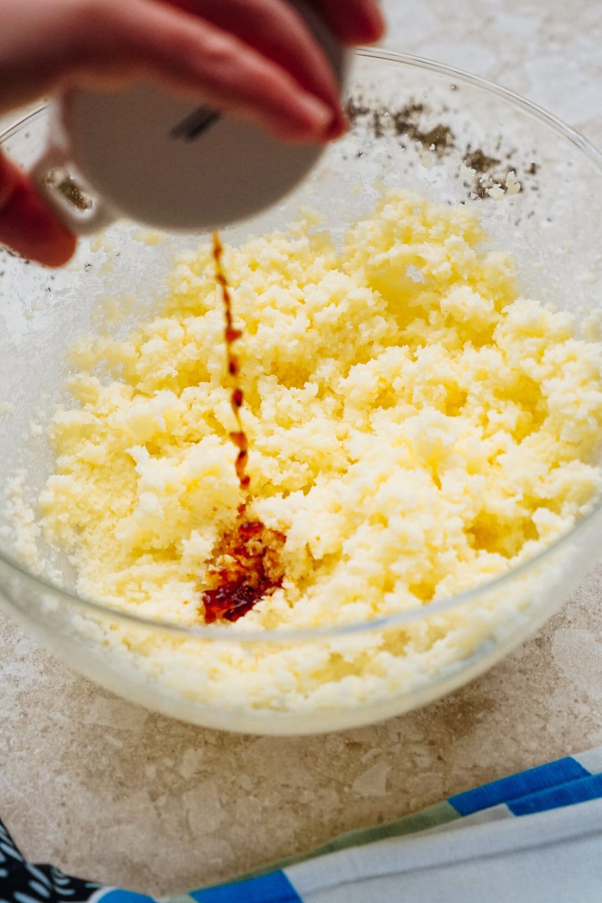 Hand pouring vanilla extract into a bowl of creamed butter and sugar.