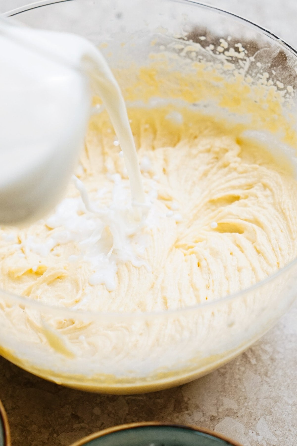 Milk being poured into a mixing bowl containing a yellow batter.