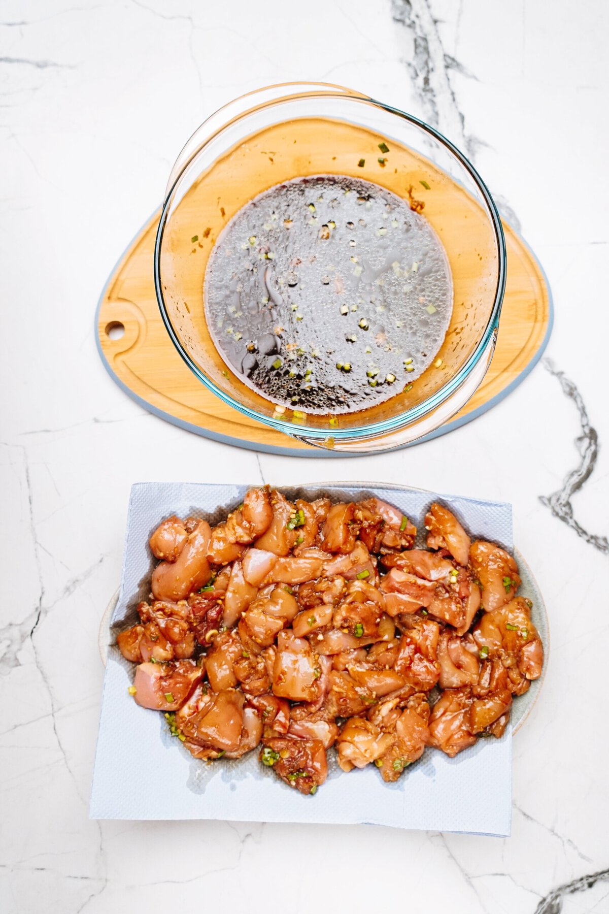 Marinated diced Korean chicken pieces on a paper towel, placed on a white marble counter, with an empty marinade bowl nearby.