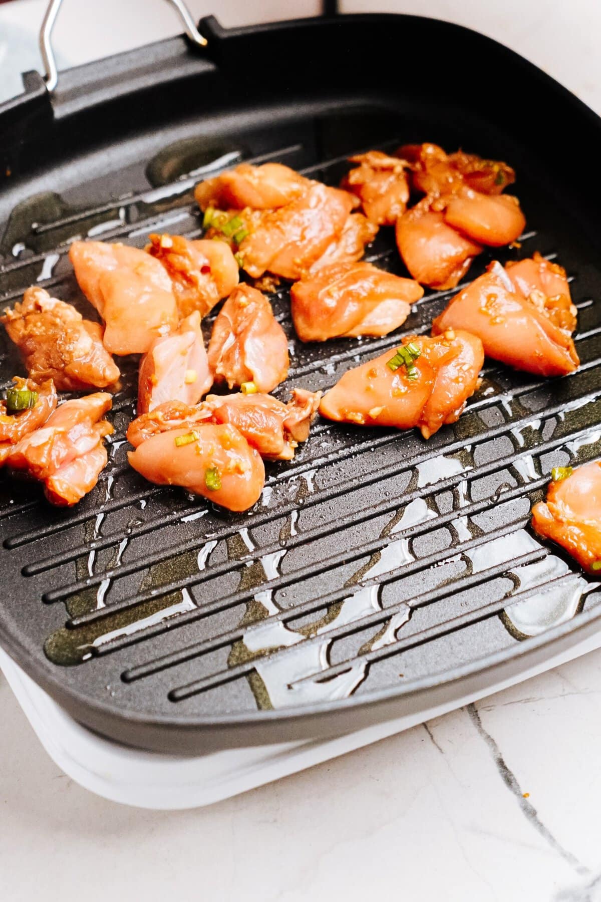 Pieces of marinated Korean chicken are placed on a heated grill pan, cooking on a stovetop.