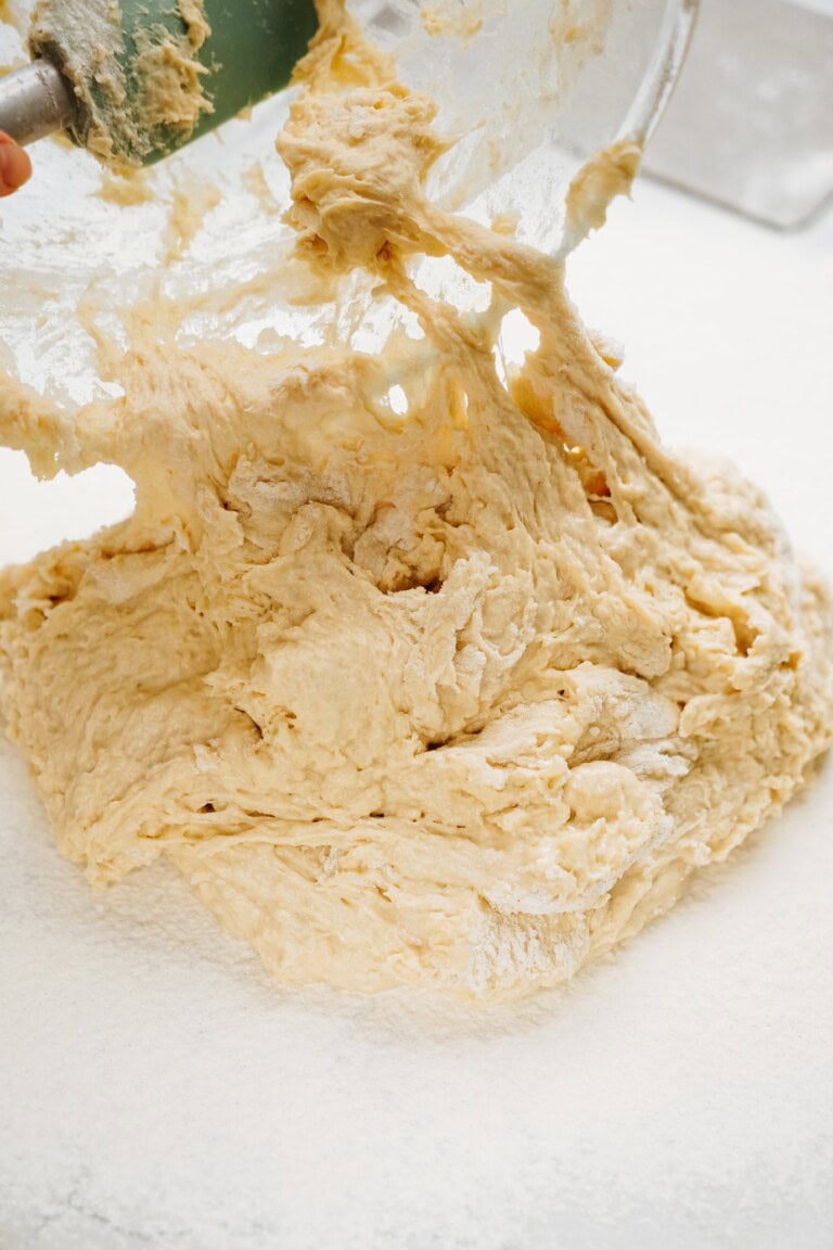 A bowl of dough destined for cinnamon rolls is poured onto a floured surface for kneading.