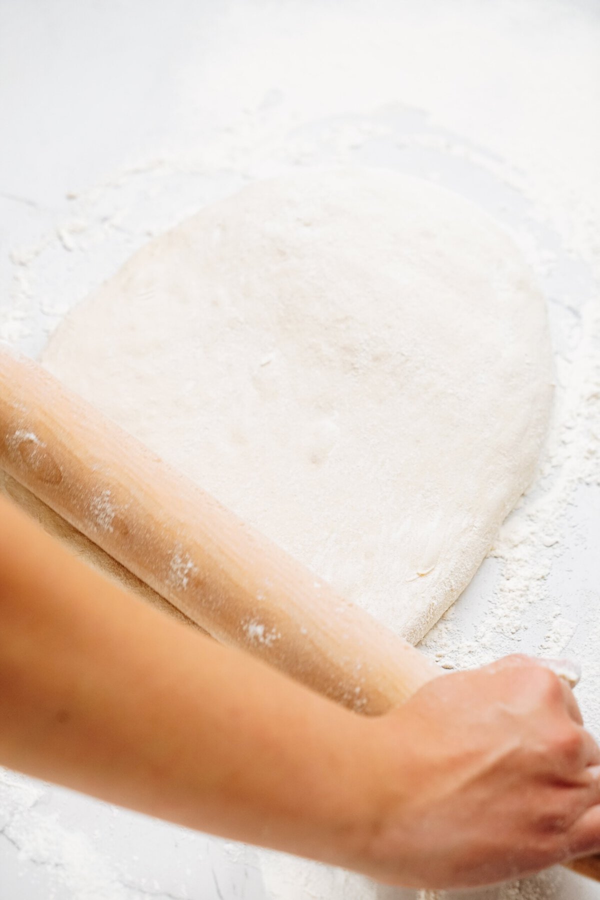 A hand uses a rolling pin to flatten dough on a floured surface, preparing it for delicious cinnamon rolls.