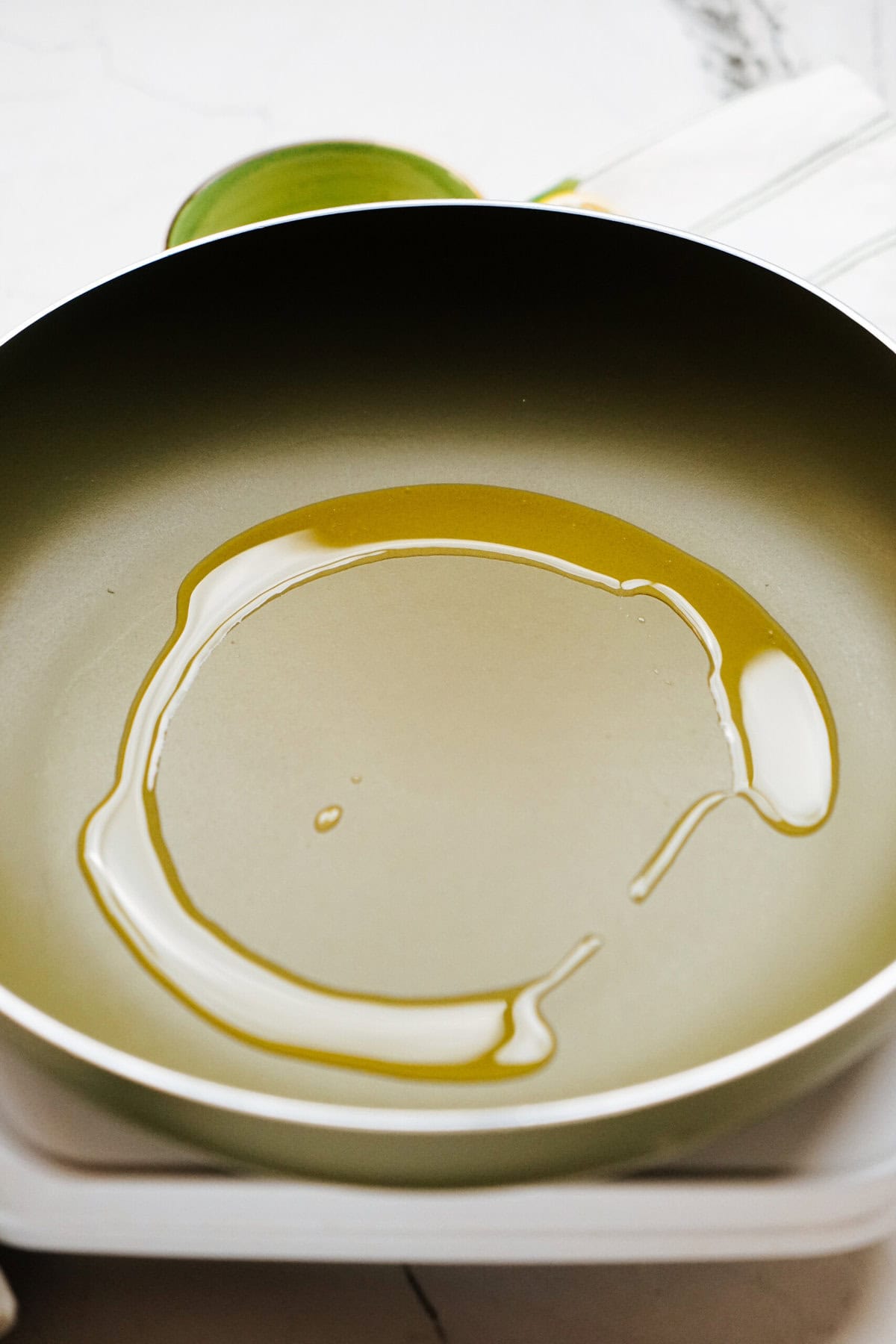 A frying pan with a thin layer of oil spread evenly across the surface on a stovetop.