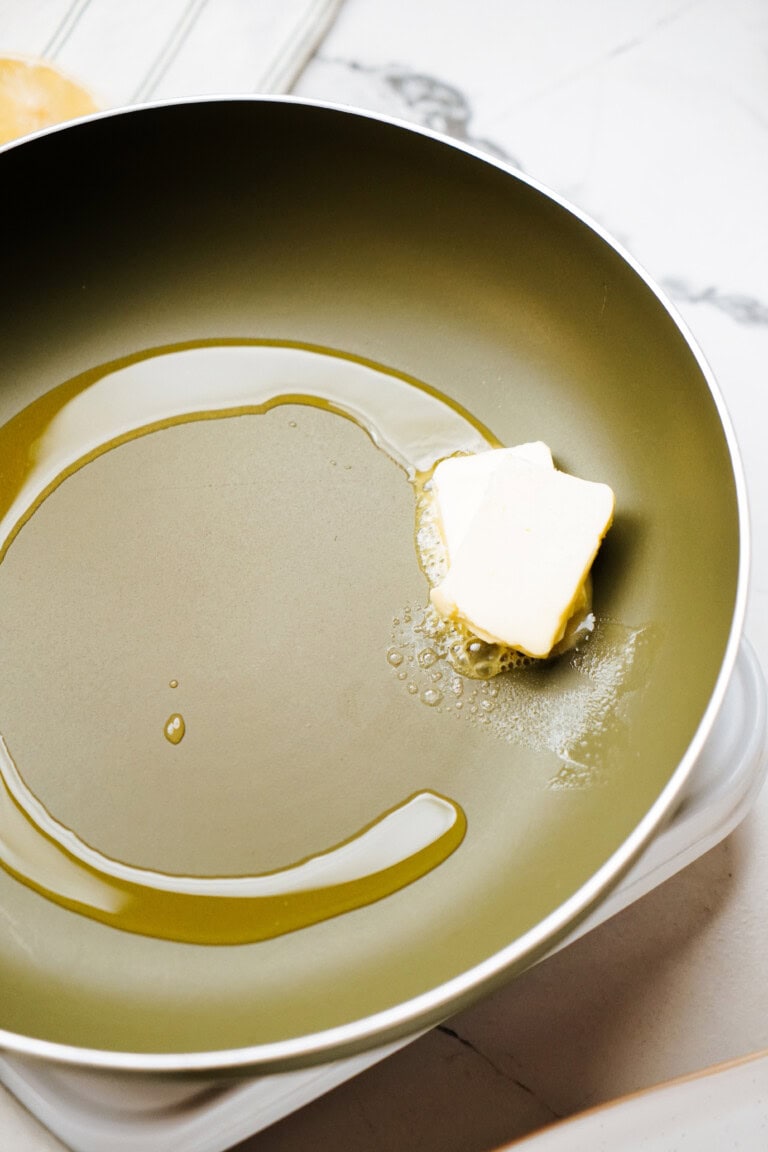 Two slices of butter melting in a frying pan with some oil on a stove.