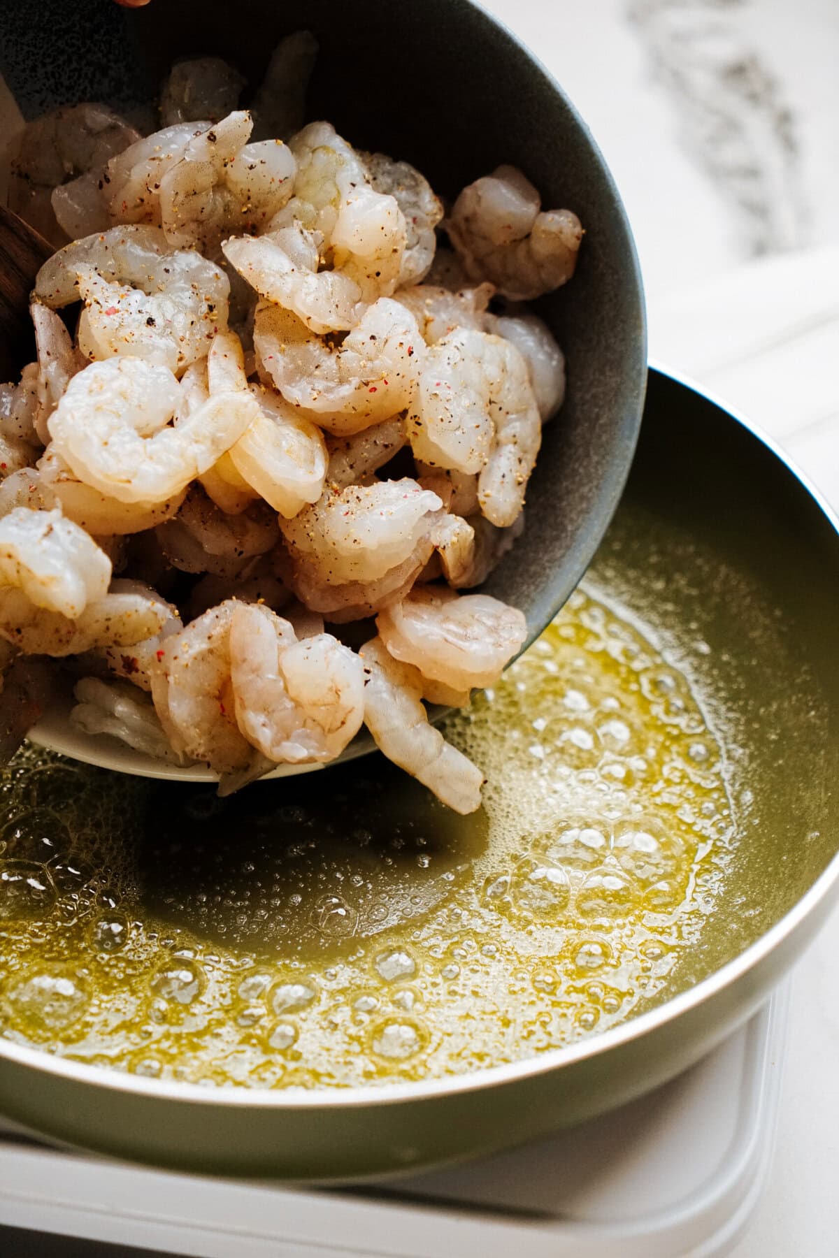 Raw shrimp being poured from a bowl into a hot pan with melted butter.