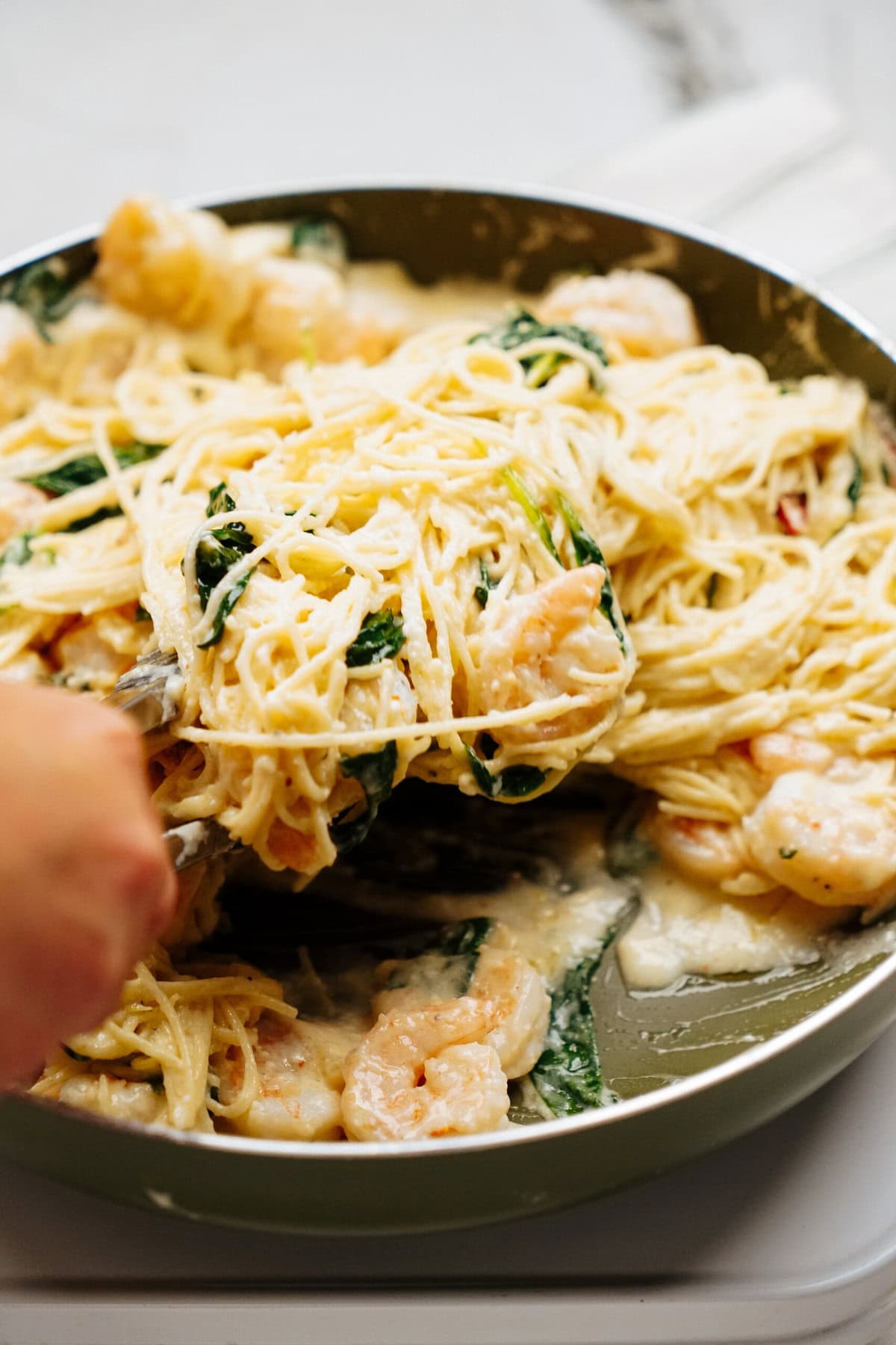 A pan of creamy pasta with shrimp and spinach being stirred with a utensil.