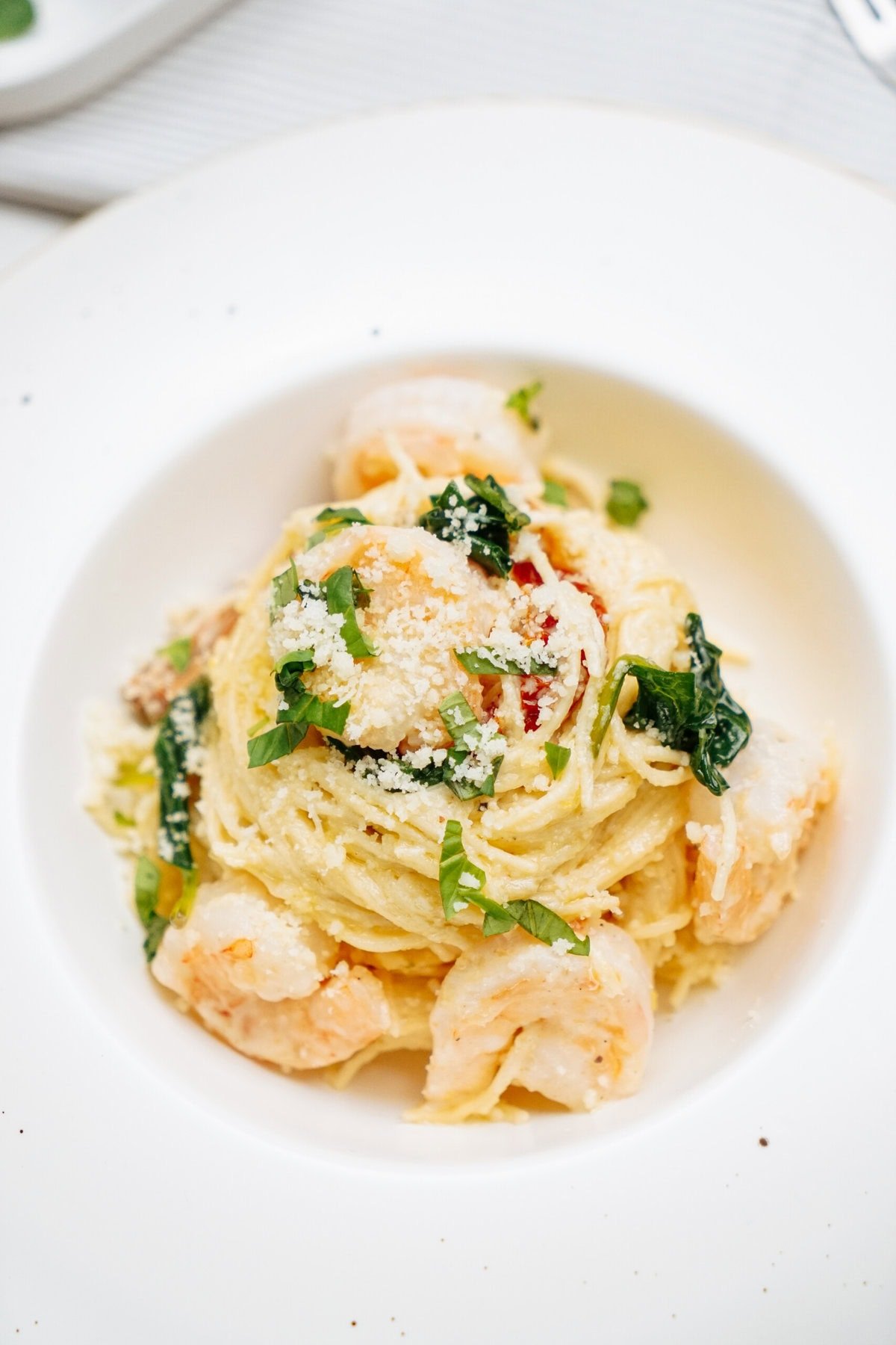 A plate of shrimp pasta garnished with grated cheese and fresh herbs.