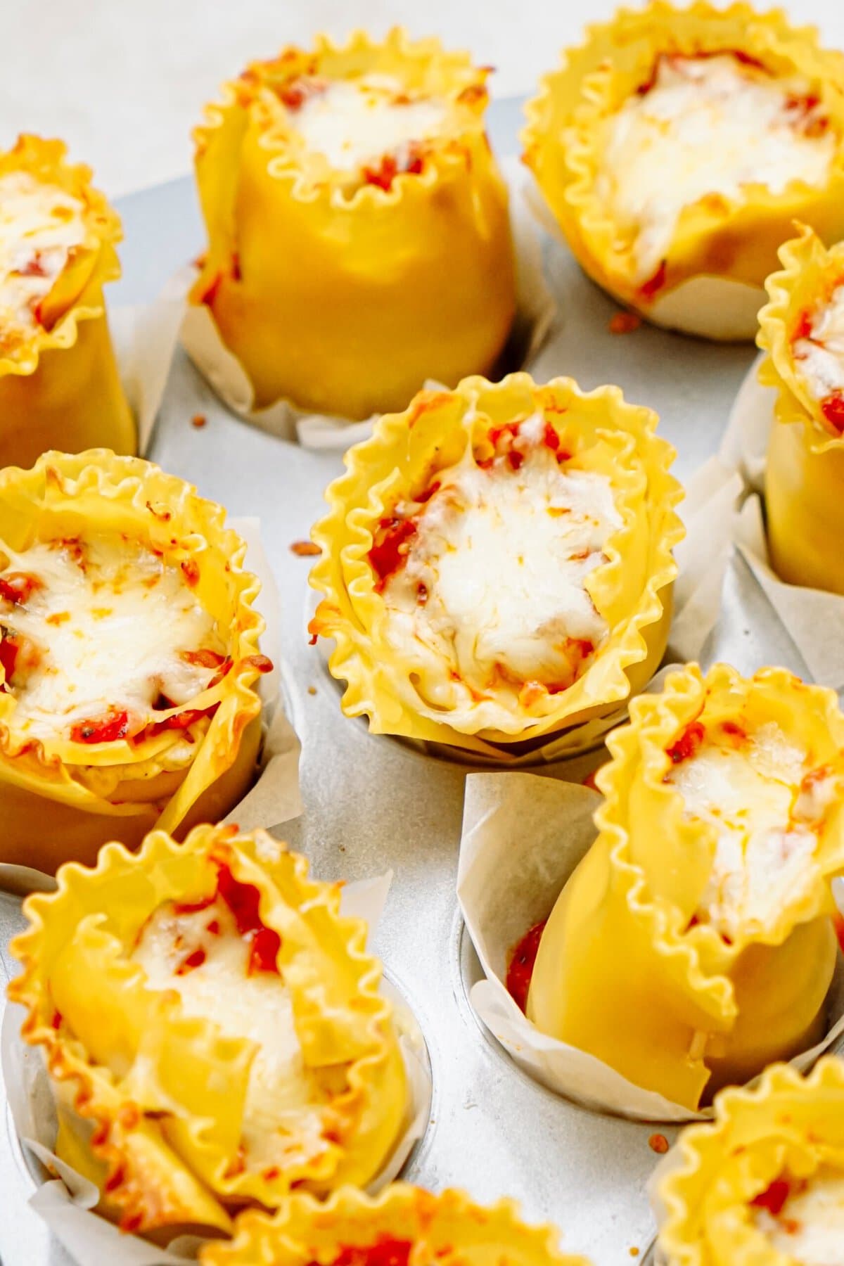 A close-up of lasagna cups filled with cheese and tomato sauce, topped with melted cheese, and arranged in paper liners.