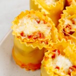 Close-up of five lasagna roll-ups filled with cheese and tomato sauce, served on a white plate. These delightful lasagna roll-ups resemble tasty lasagna cups, perfect for individual servings.